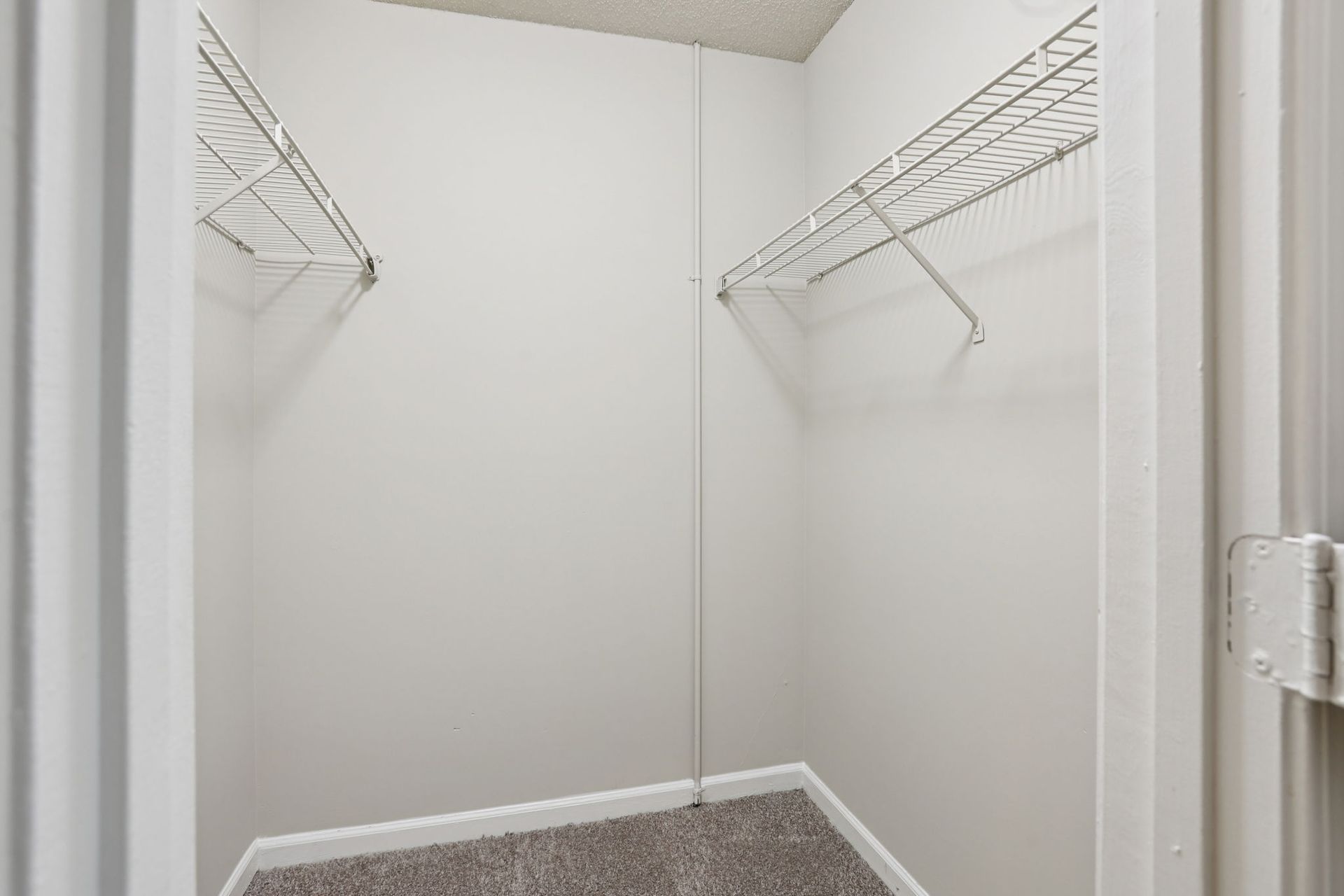 A walk-in closet with beige walls, gray carpet, and white wire shelving on two sides.