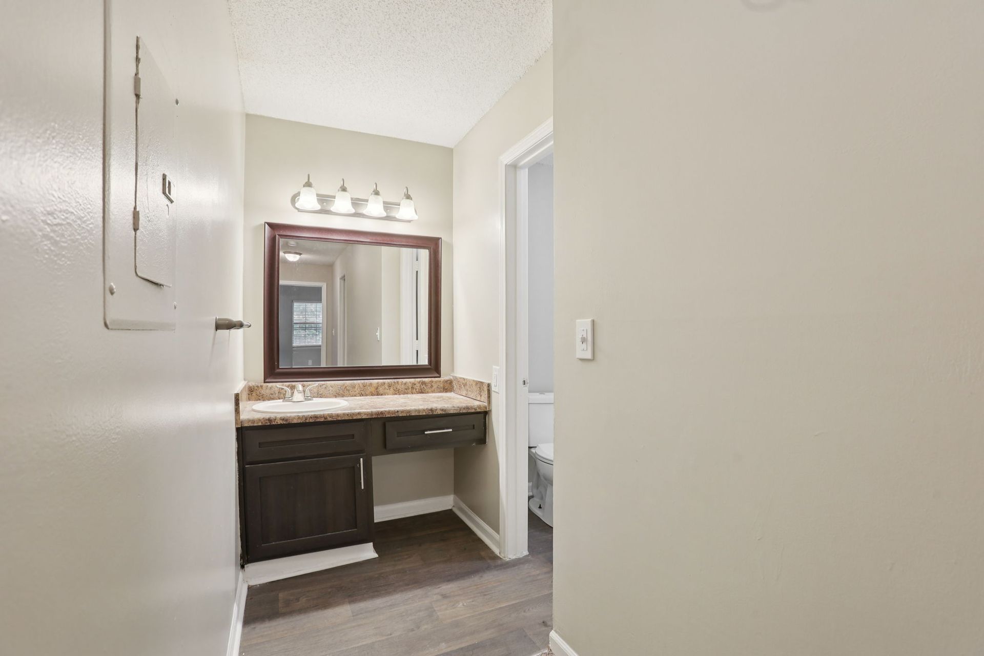 A bathroom vanity with a dark wood cabinet, granite countertop, and mirror, leading to a separate toilet area.