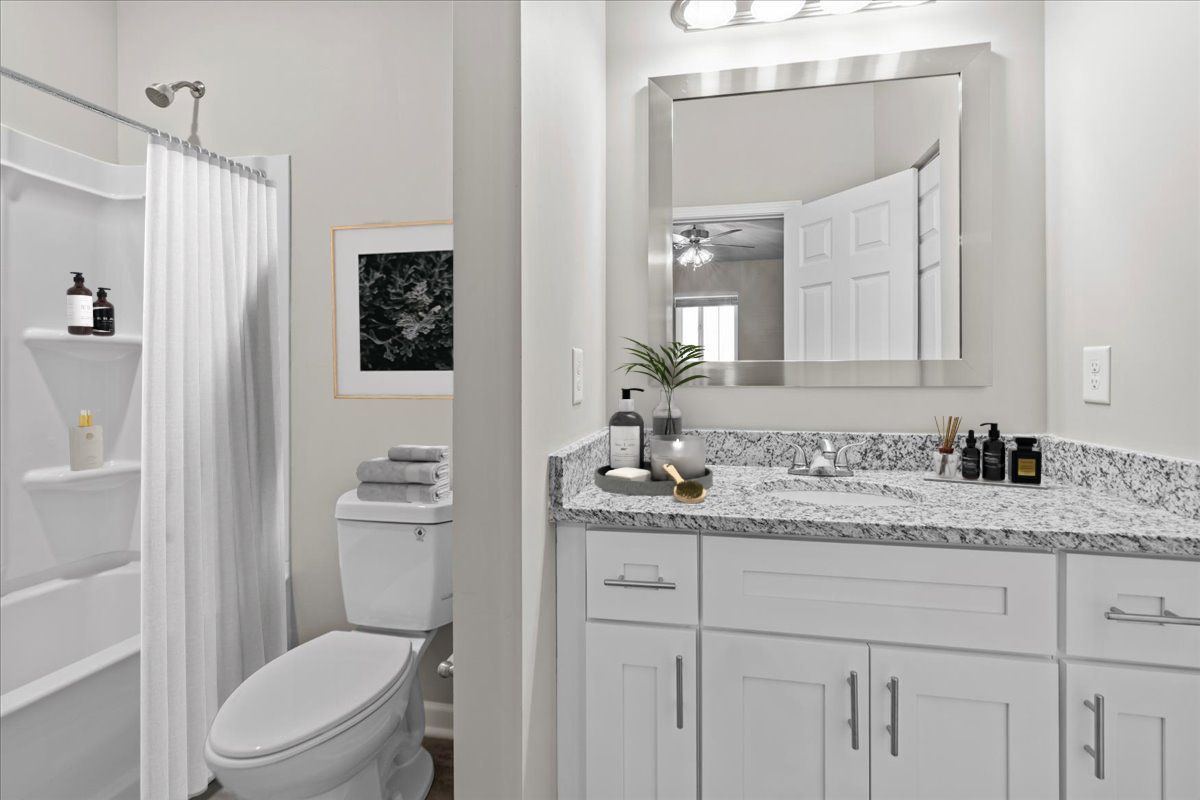 A modern bathroom with a white vanity, speckled granite countertop, toilet, and a shower with a white curtain.