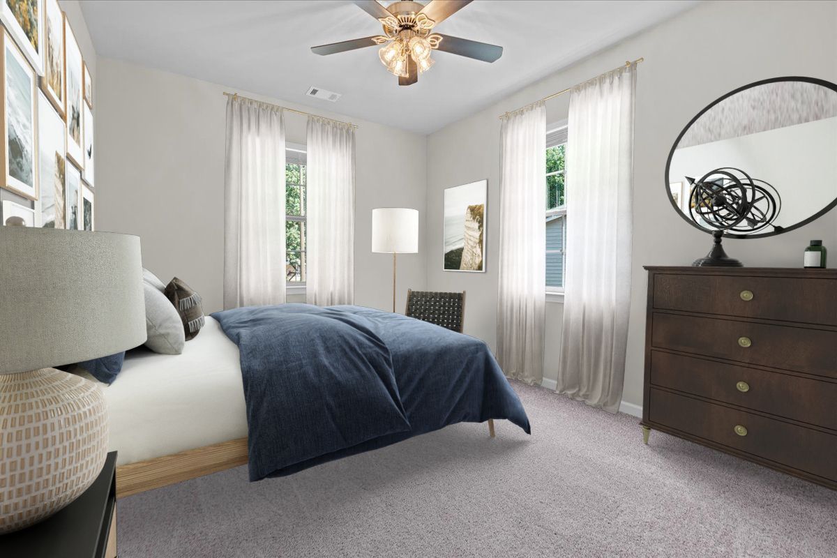 A modern bedroom with a blue bedspread, wooden dresser with a mirror, gray carpet, and white curtains.