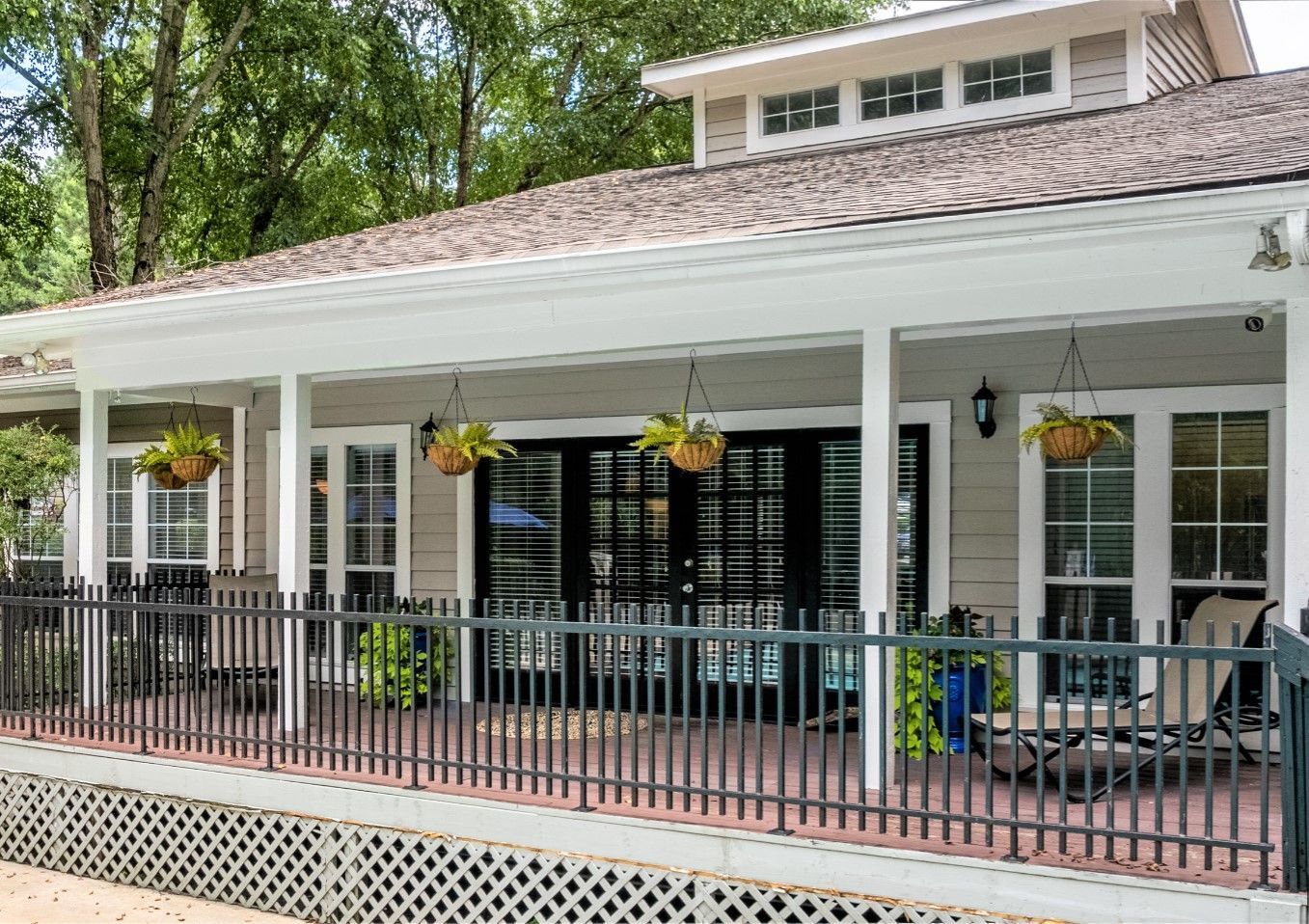 A covered porch with white columns, black doors, hanging plants, and a metal railing in front of a light-colored house.