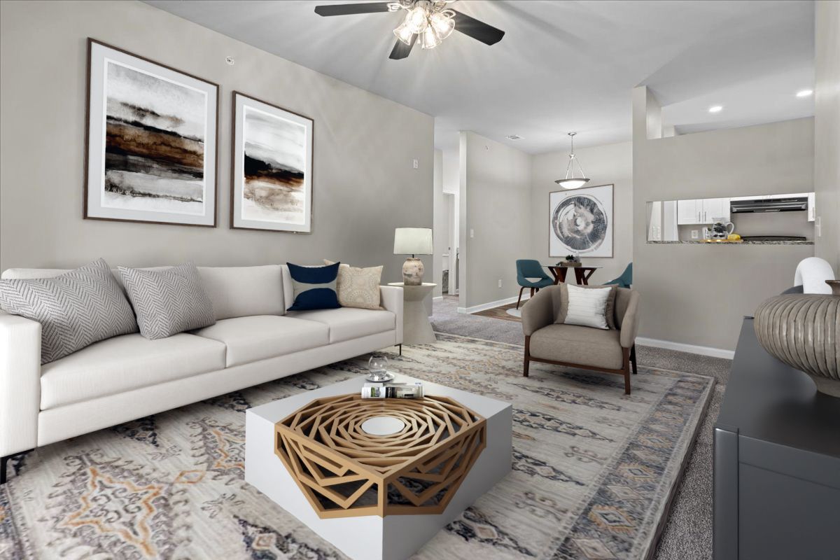 A neutral-toned living room features a beige sofa, patterned area rug, geometric coffee table, and an armchair.