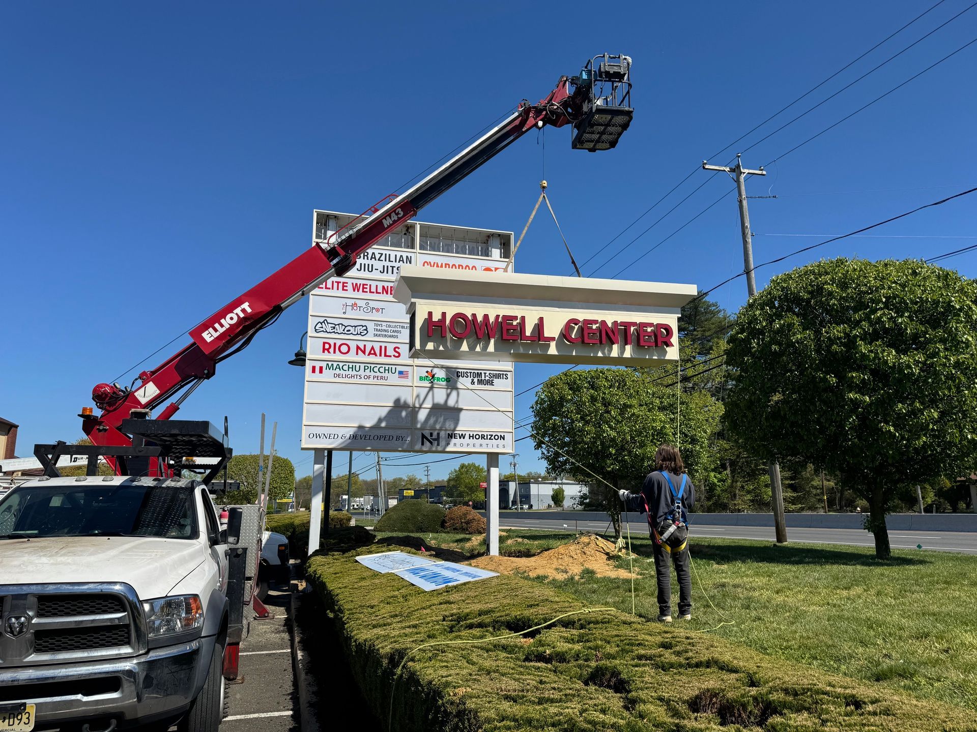 Worker on a cherry picker installing a large sign beside a road on a sunny day.