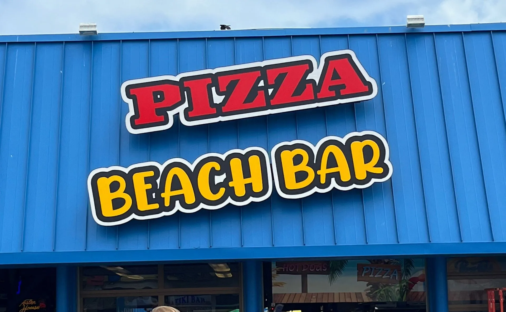 Blue storefront sign reading “PIZZA BEACH BAR” in red and yellow letters