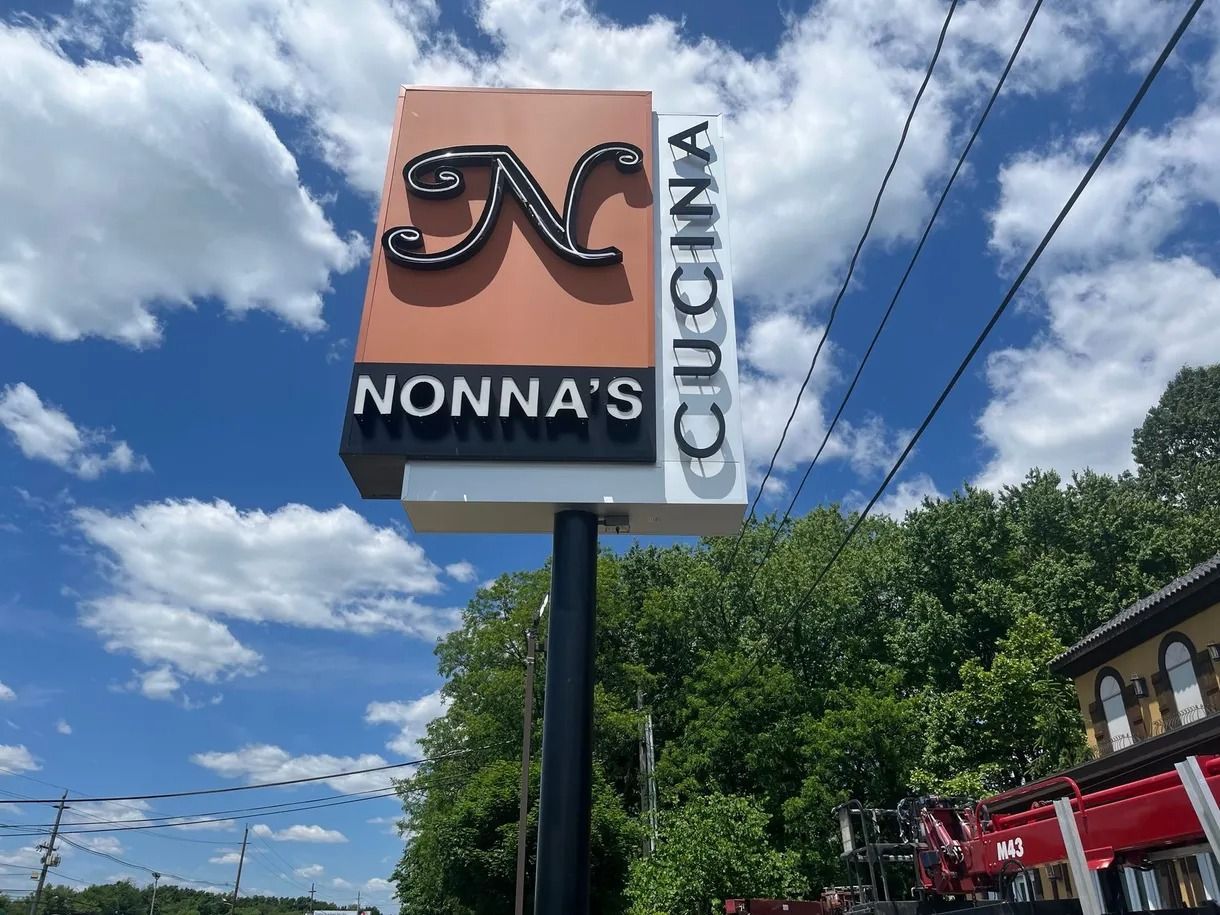 Nonna’s Cucina storefront sign with a chef-hat logo against a blue sky with clouds