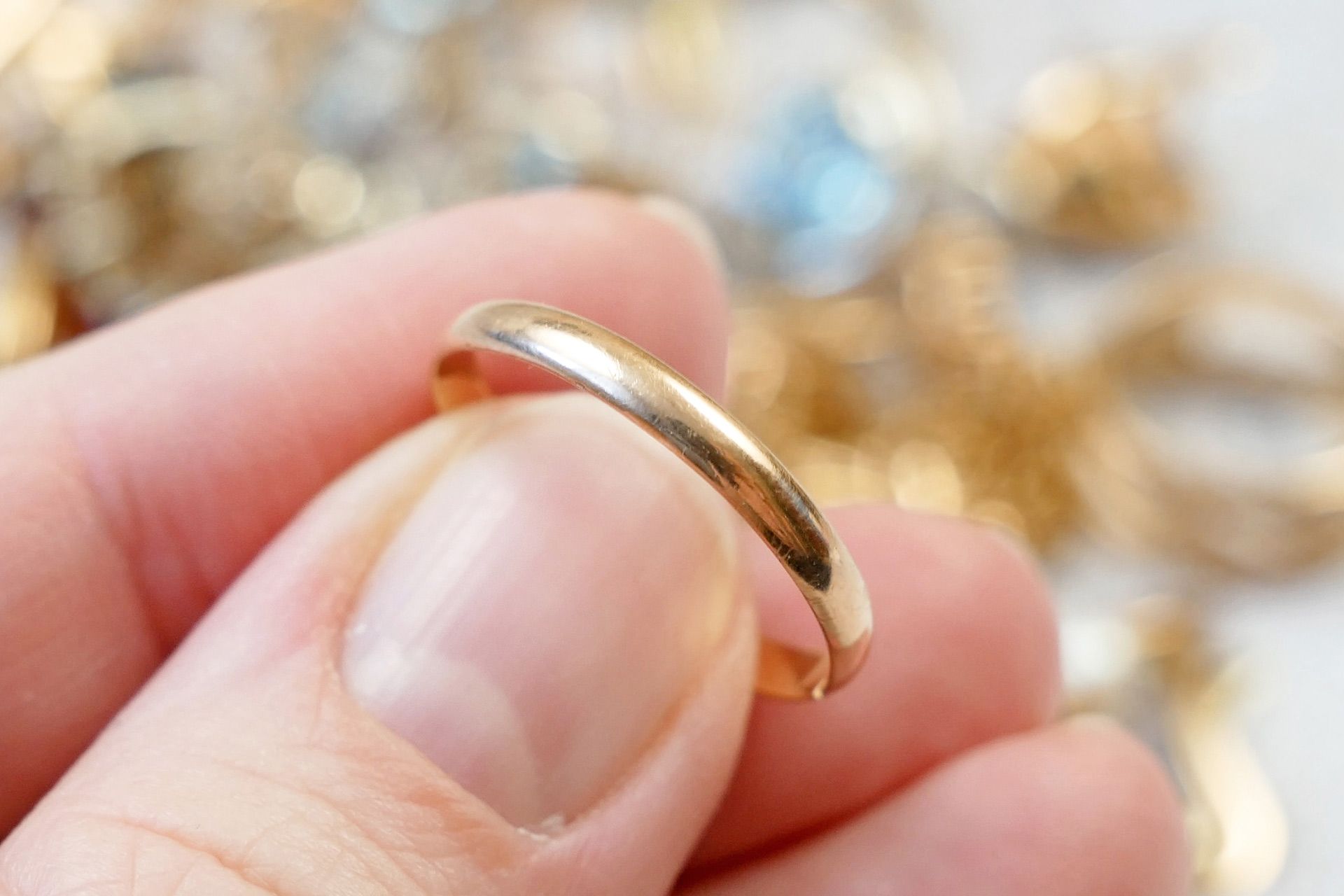 A hand holding a shiny gold ring against a blurred jewelry display background