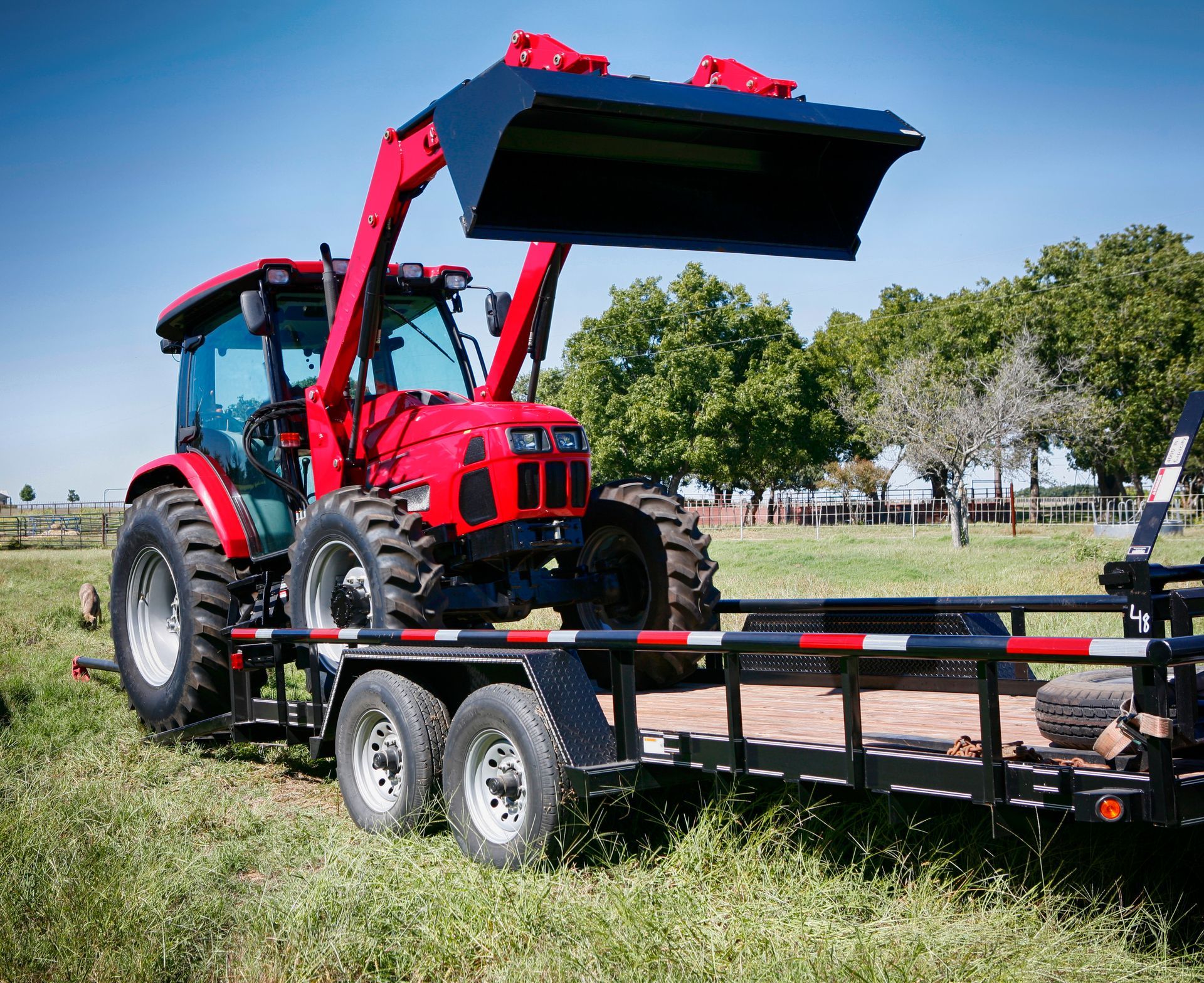 Red tractor loaded on a flatbed trailer in a grassy field. Red tractor loaded on a flatbed trailer in a grassy field.