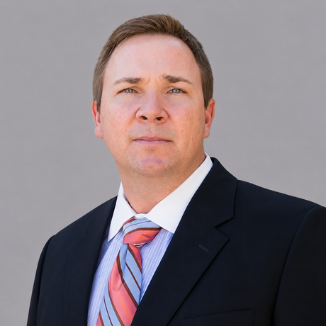 A man in a suit and tie stands in front of a brick wall