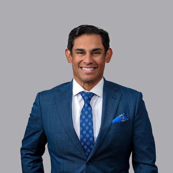 A man in a suit and tie is smiling in front of a brick wall.