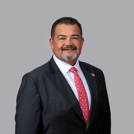 A man in a suit is smiling in front of a brick wall.
