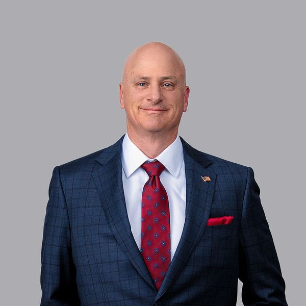 A man in a suit and tie is standing in front of a brick wall.