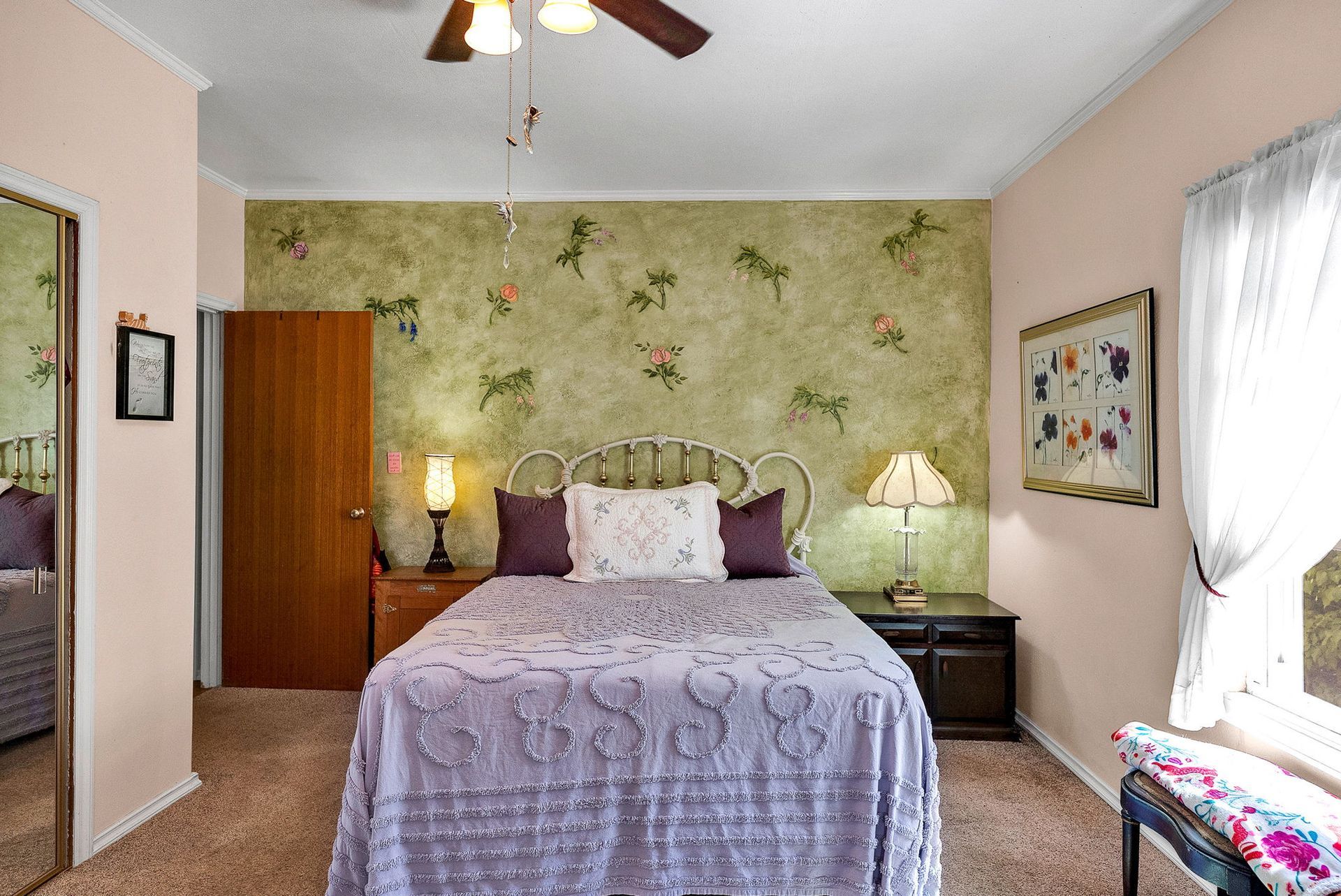 Cozy bedroom with floral wallpaper, a bed, nightstands, and sunlight through a window