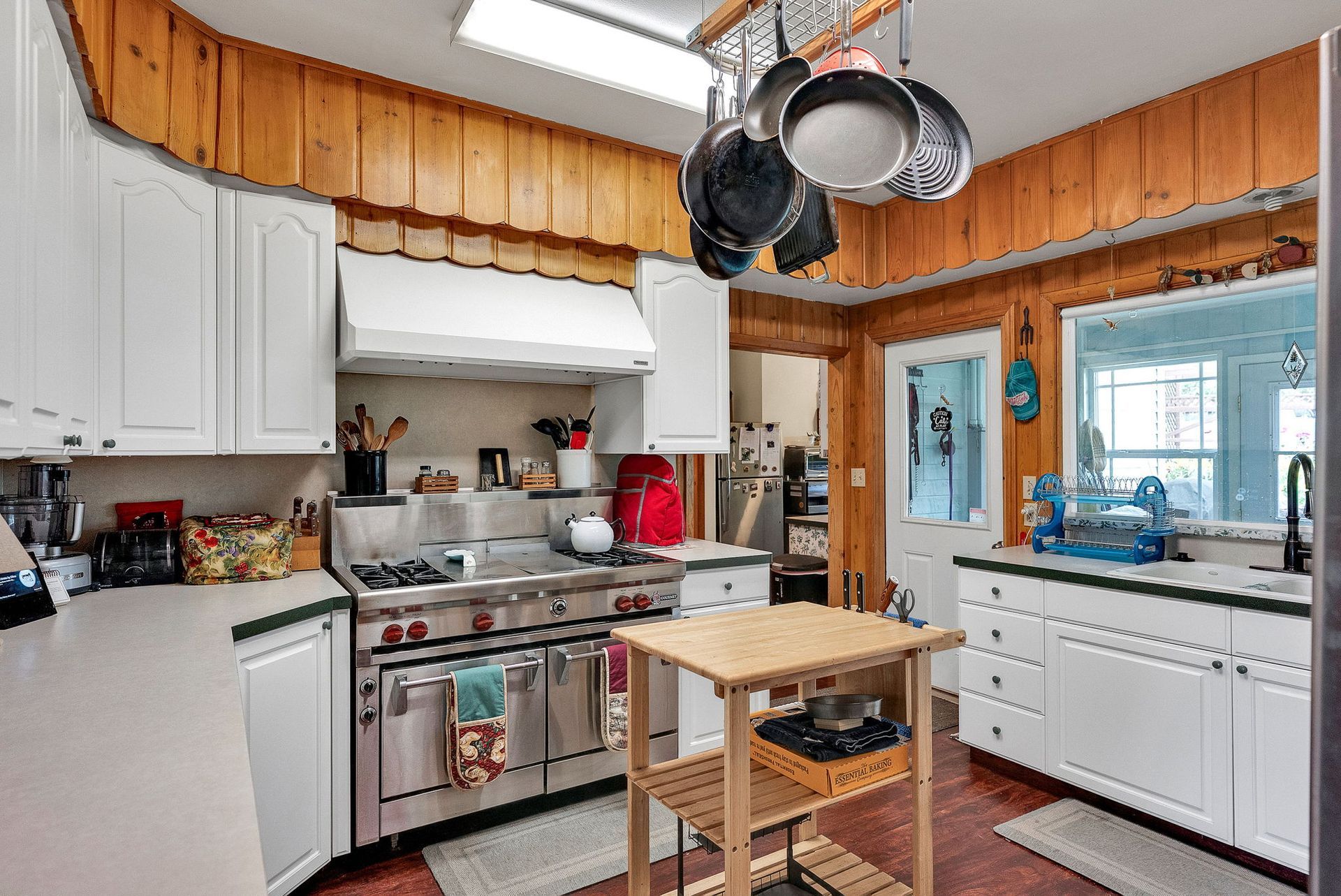 Bright kitchen with white cabinets, stainless stove, hanging pans, and a small wooden island.