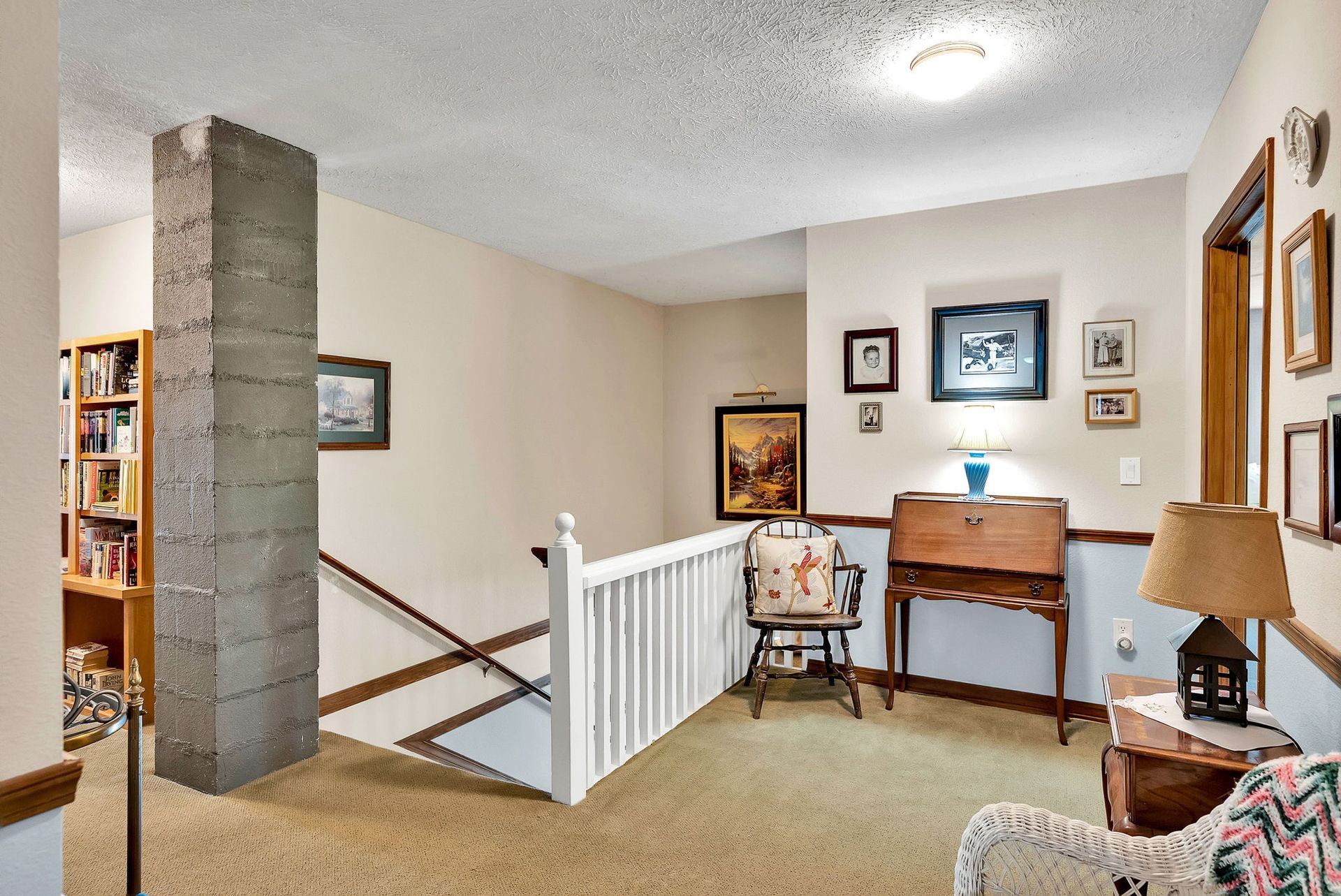 Stair landing with white railing, desk and chair, framed art, and beige walls in a cozy home interior