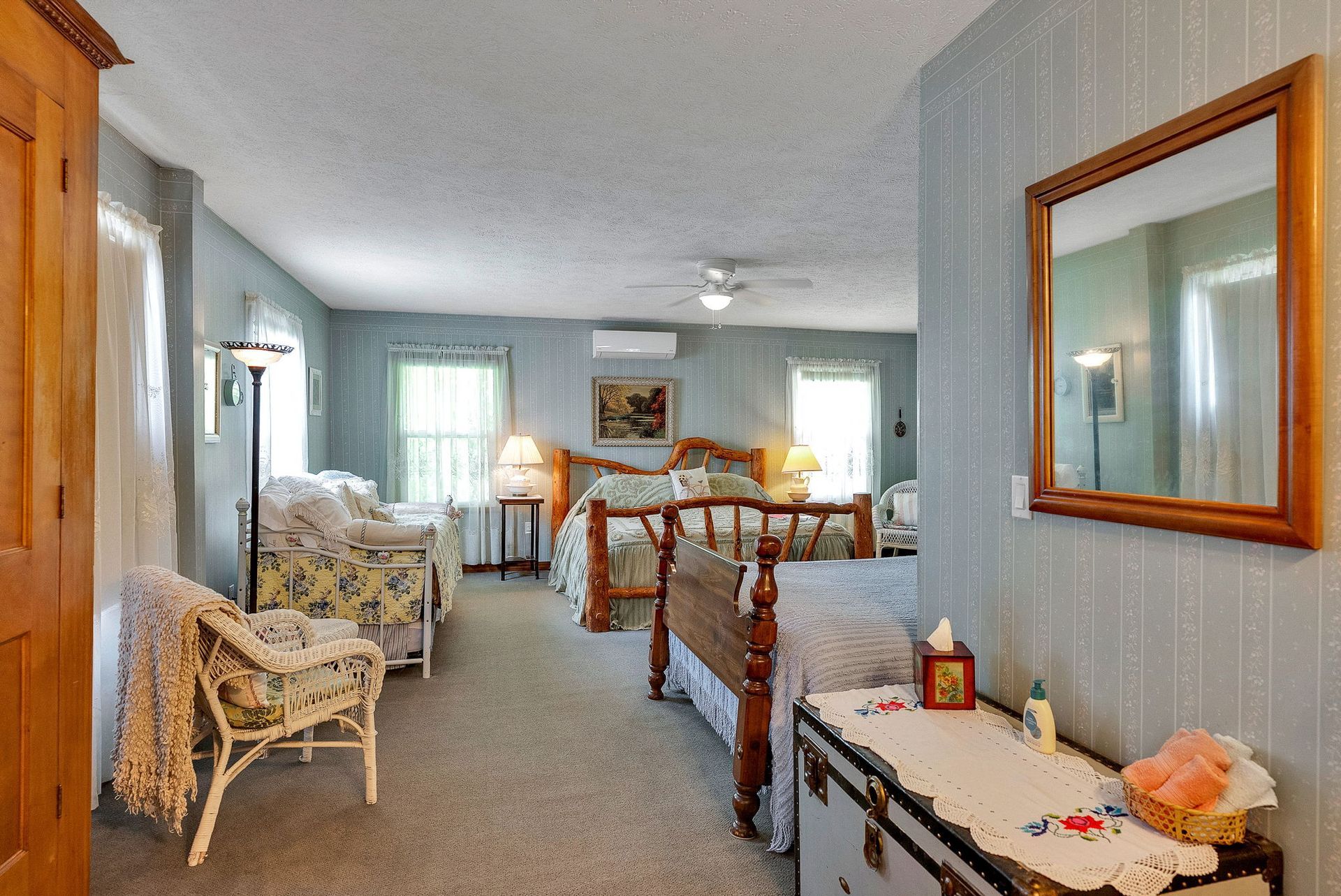Cozy living room with wicker furniture, carpeted floor, lamps, and a side table with decor and a mirror.