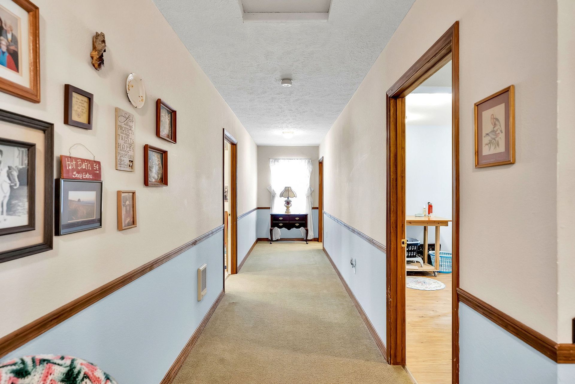 Bright hallway with framed photos on the walls and open doorways to rooms at the end.