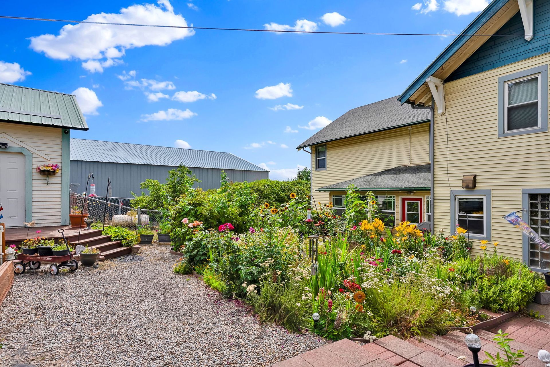 Colorful garden courtyard with gravel paths, flowers, and beige houses under a bright blue sky