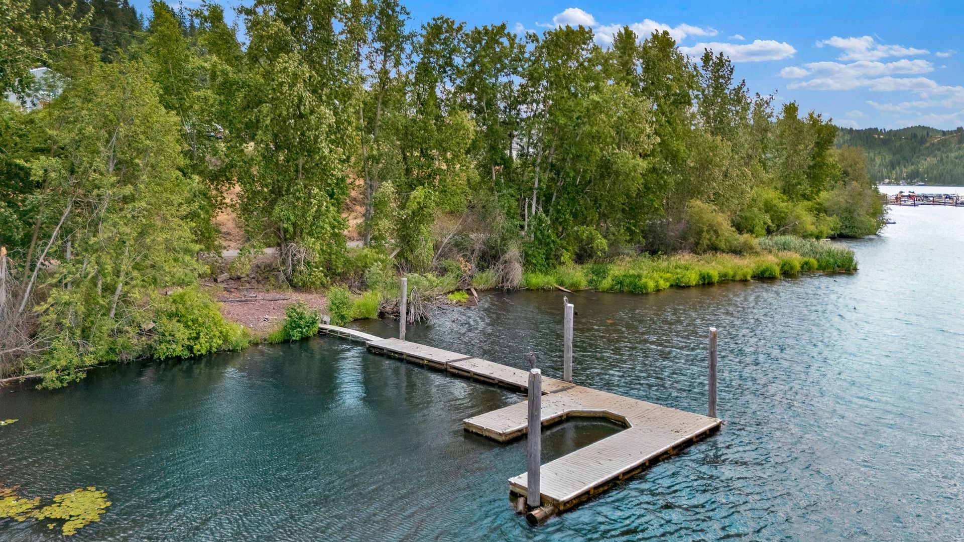 Wooden dock on a calm blue lake beside a tree-lined rocky shore