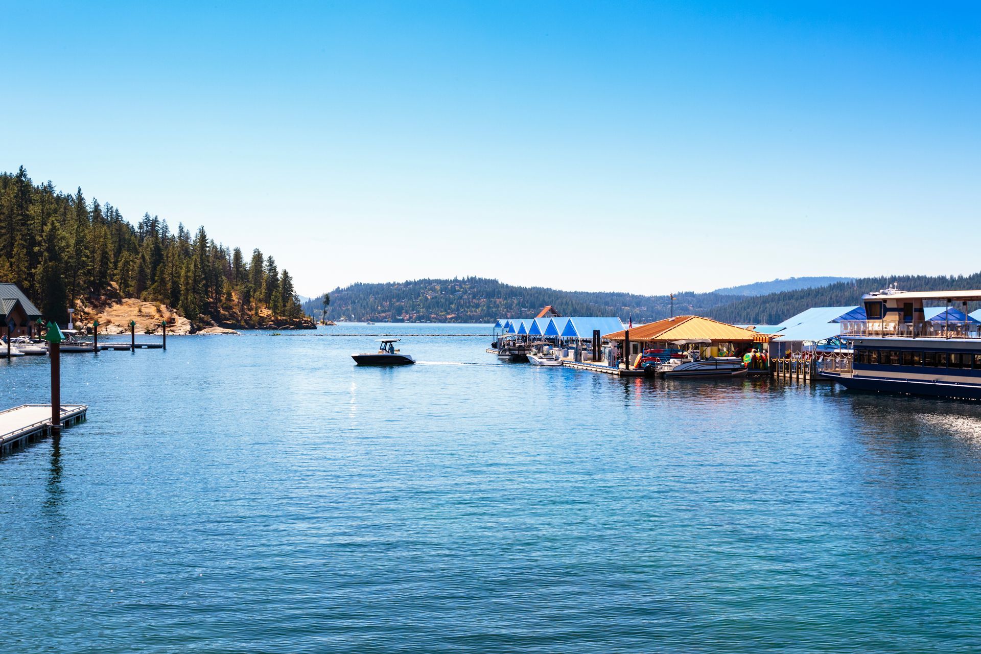 A sunny day at a mountain lake marina with a small boat, floating docks, and surrounding pine-covered hills.