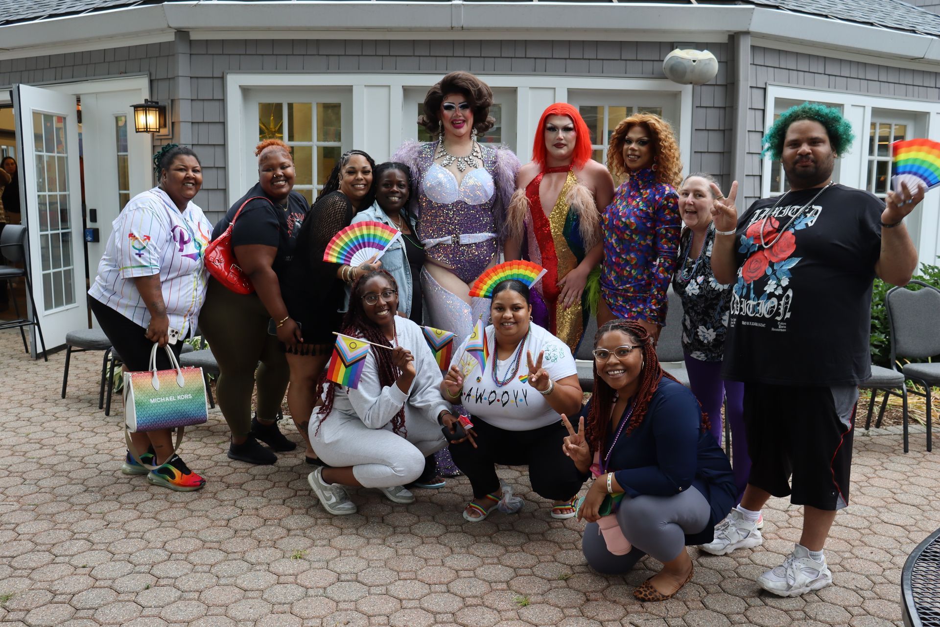 A group of people wearing rainbow-themed clothing poses together for a photo in front of a gray building.
