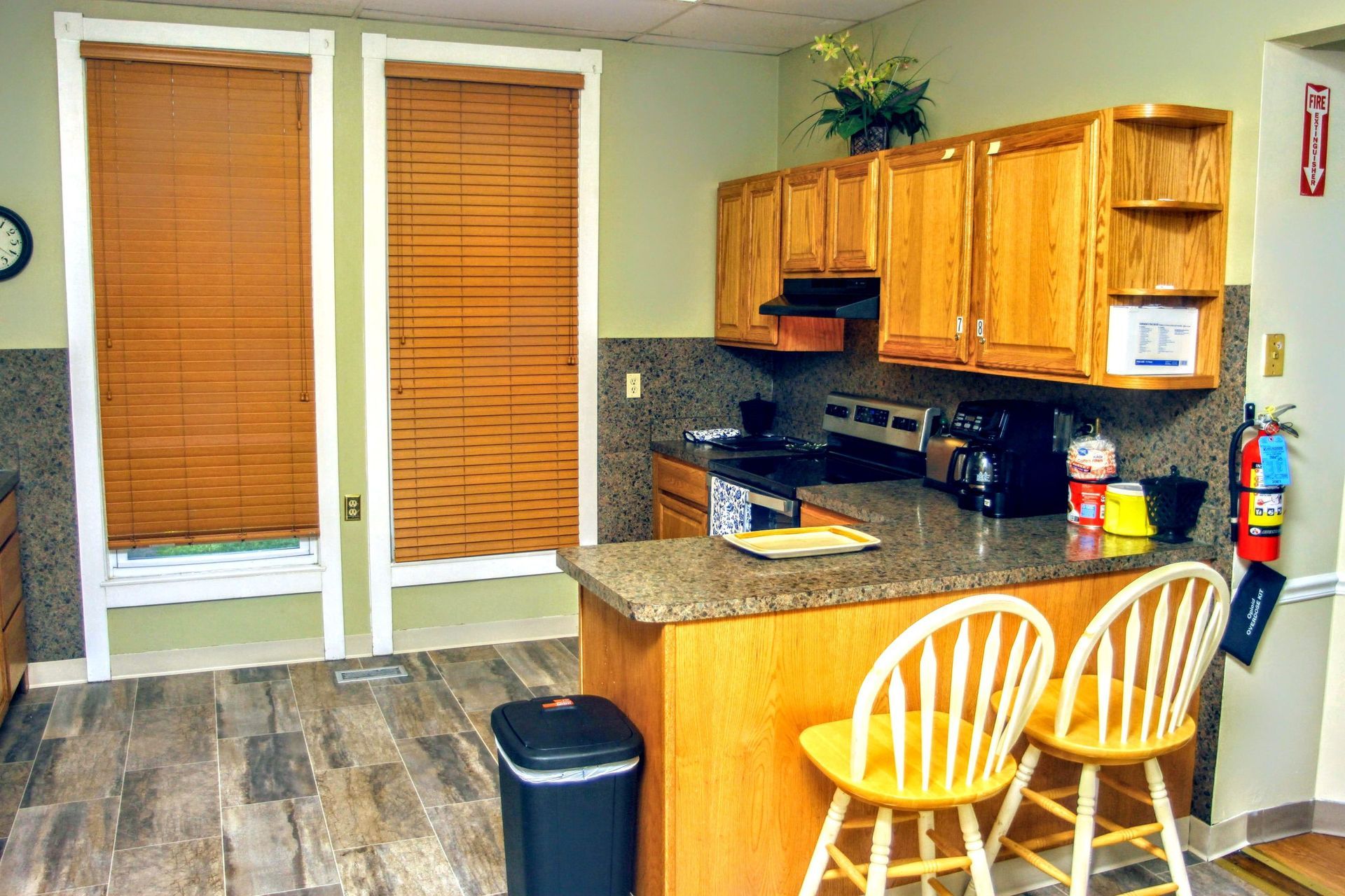 A kitchen with wooden cabinets, stools, a trash can and a fire extinguisher.