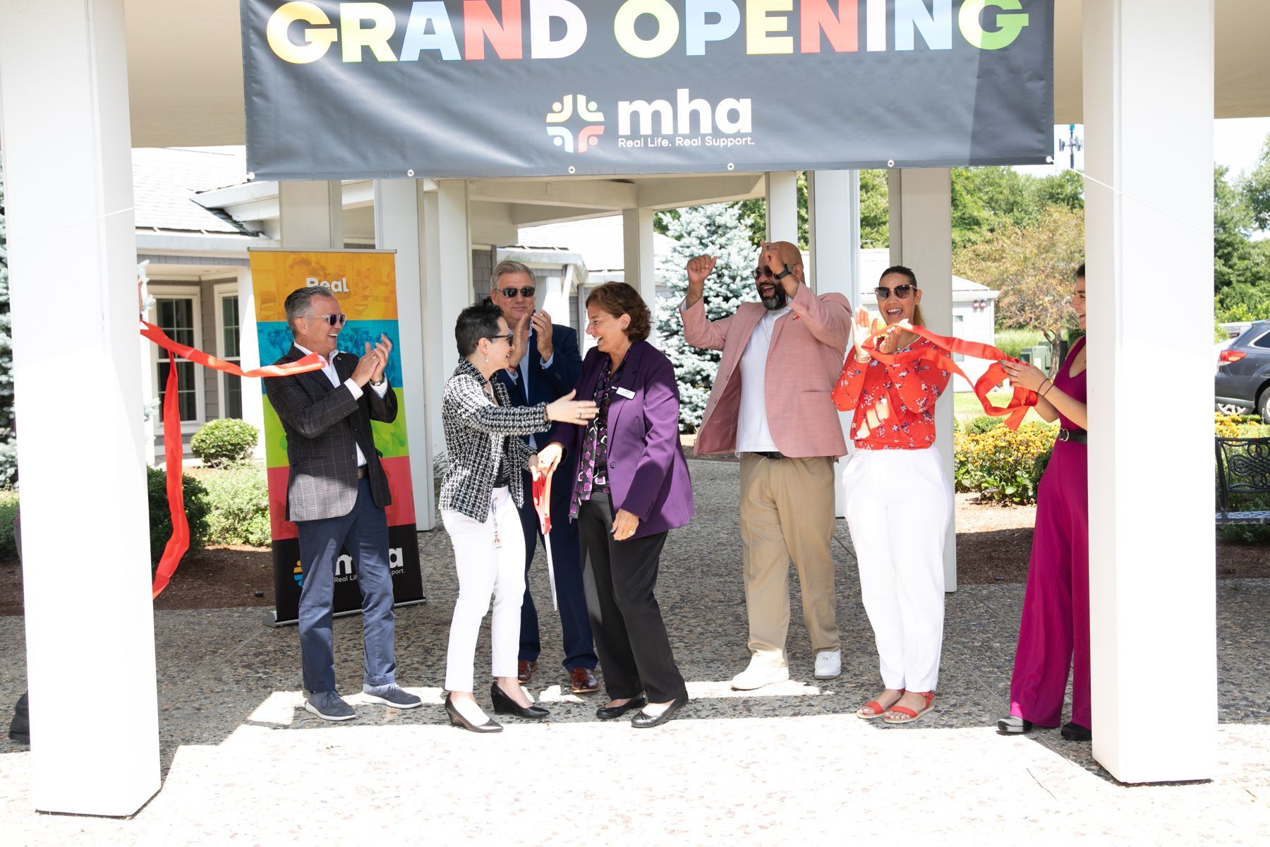 A group of people are standing under a banner that says grand opening