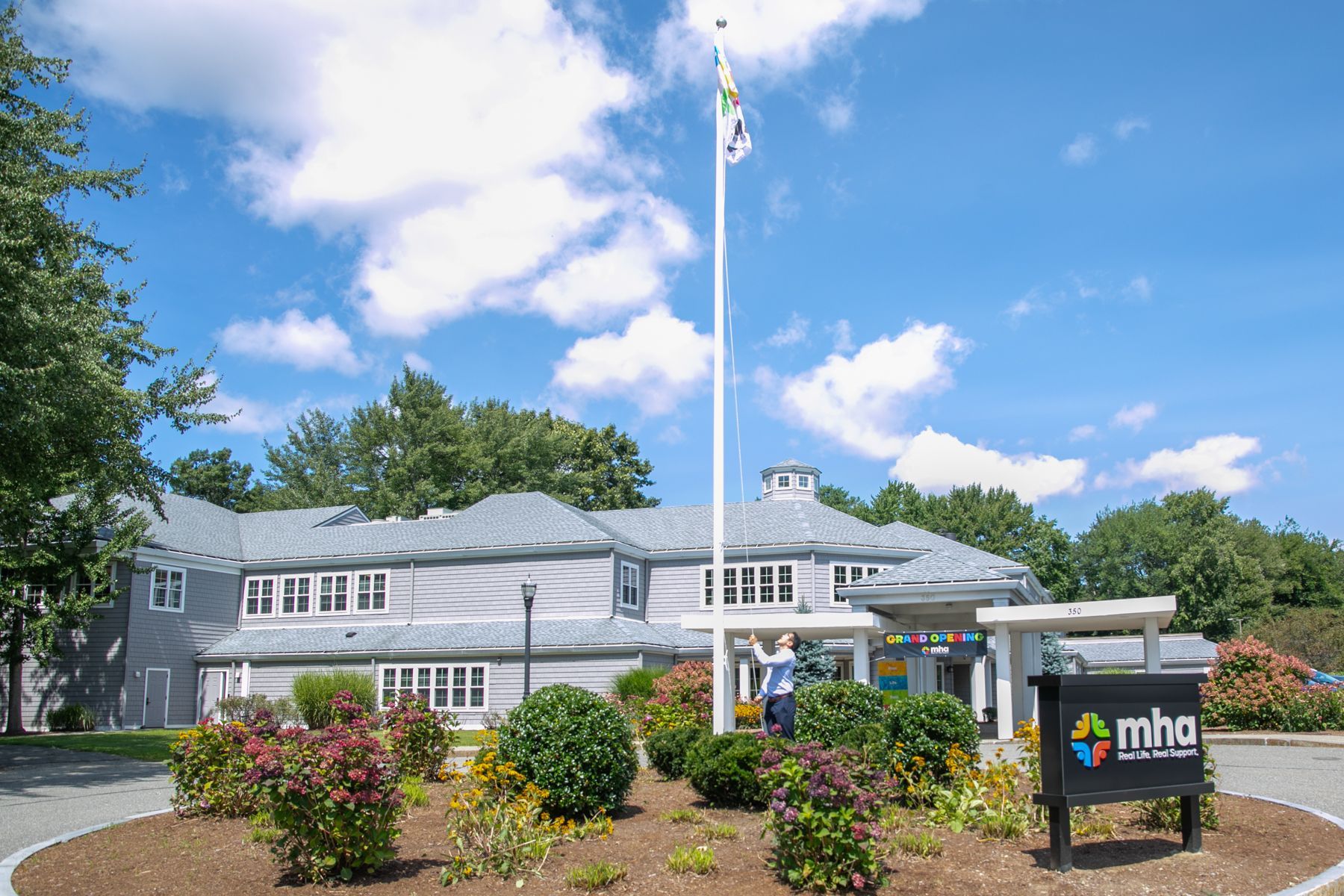 A building with a flag on top of it and a sign in front of it with MHA logo
