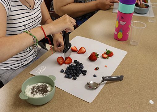 A woman is cutting strawberries and blueberries on a cutting board using an adaptive knife.