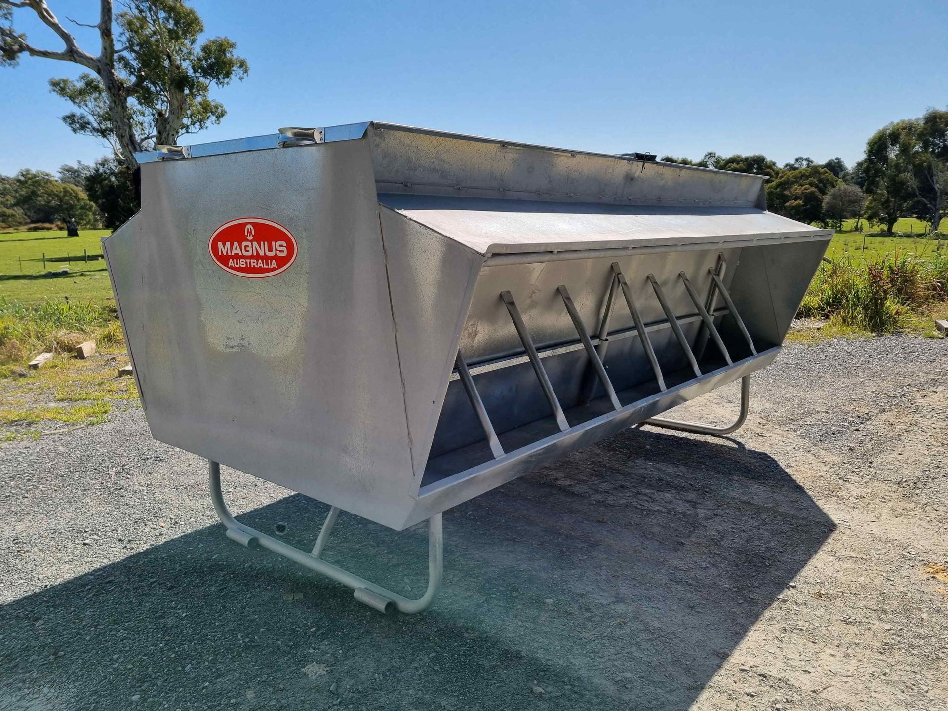 A stainless steel feeder is sitting on the ground in a field.
