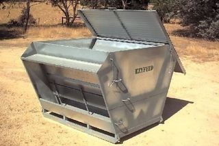 A metal container with the lid open is sitting on top of a dirt field.