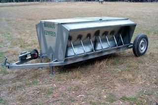 A stainless steel feeder is sitting on top of a trailer in a field.