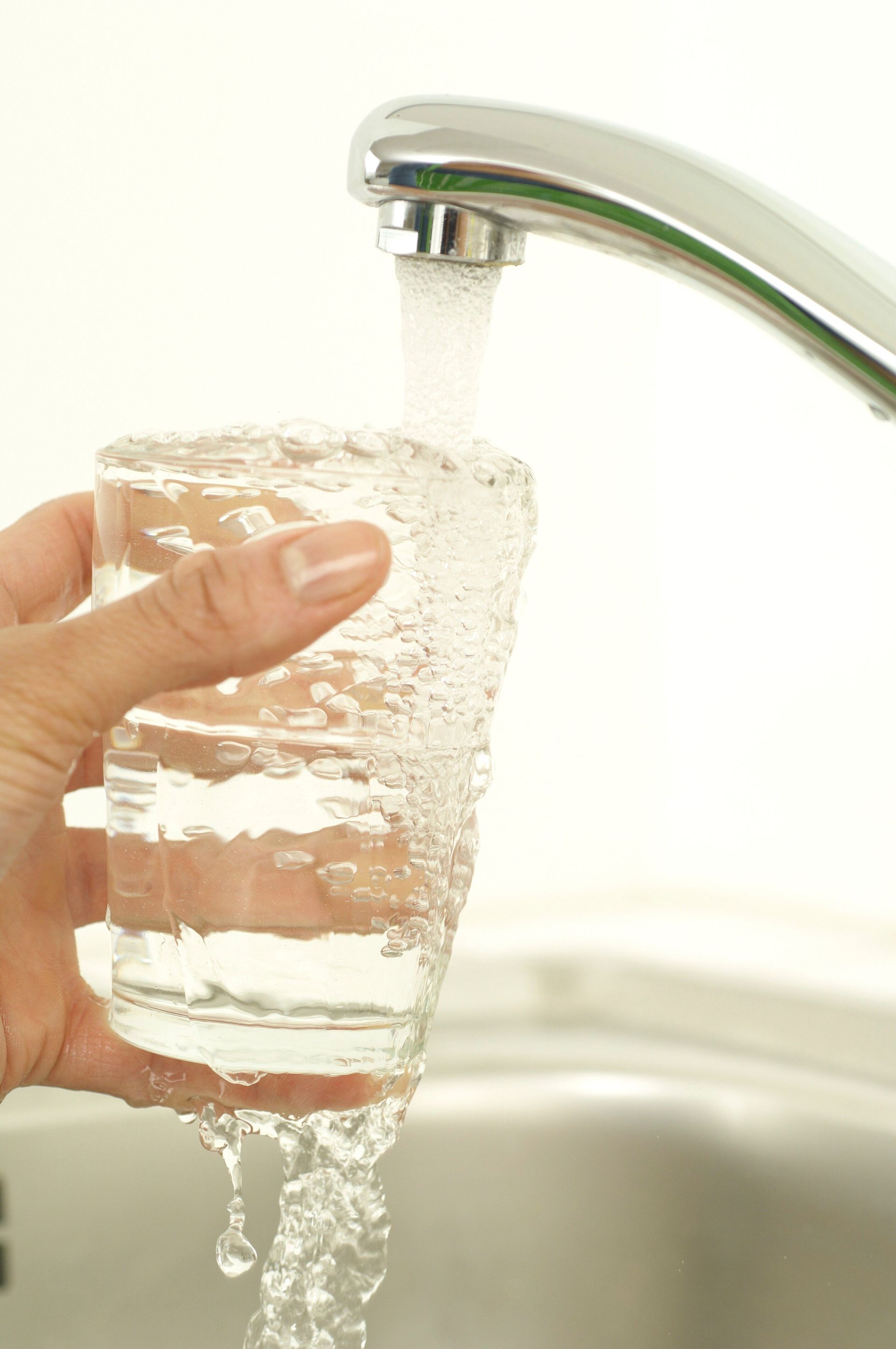 Hand holding a clear glass under a running kitchen faucet, filling it with water