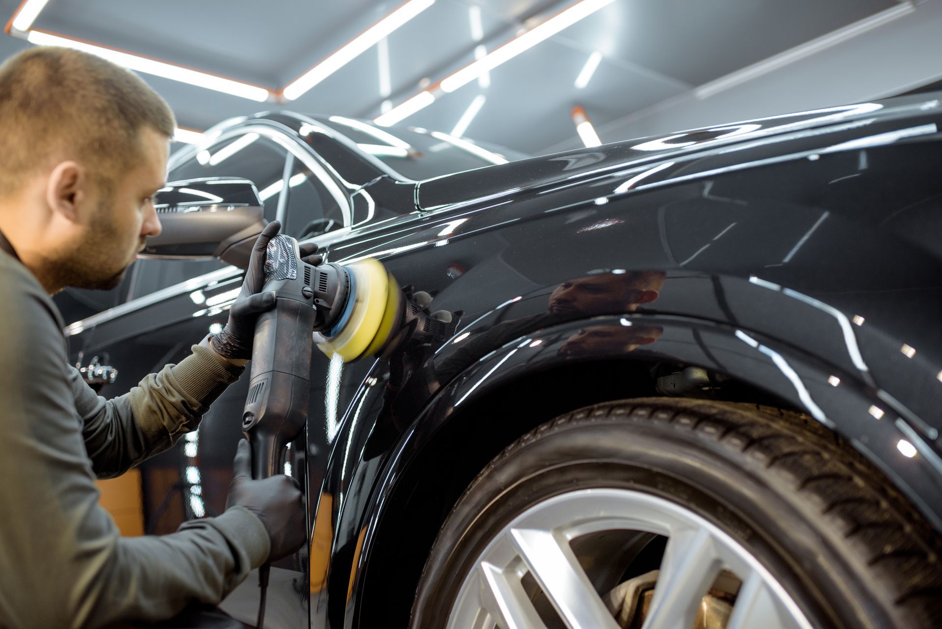 A man is polishing the fender of a black car.