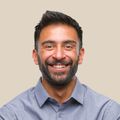 A man with a beard is smiling with his arms crossed.