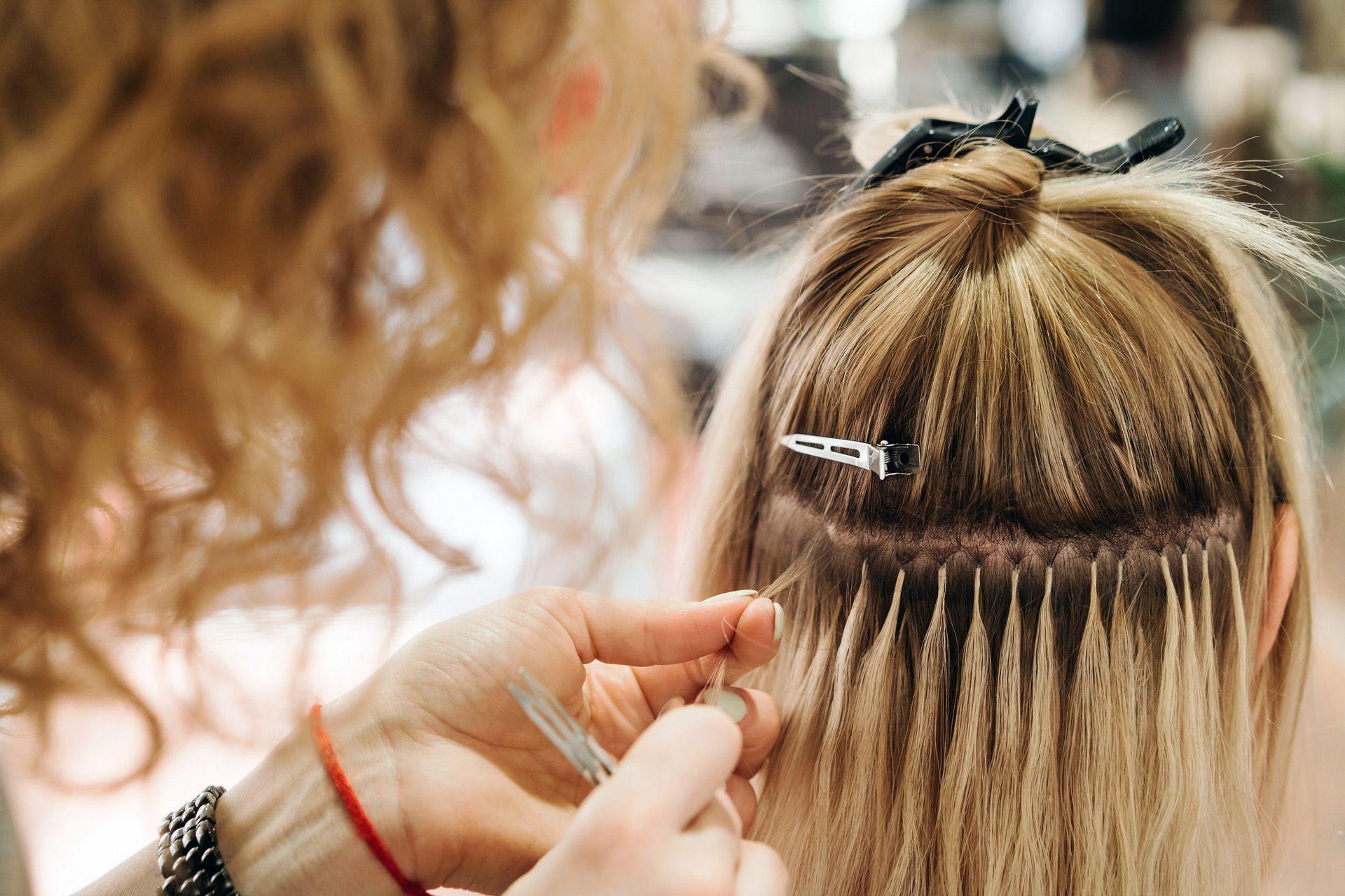 A woman is getting her hair extensions done by a hairdresser.