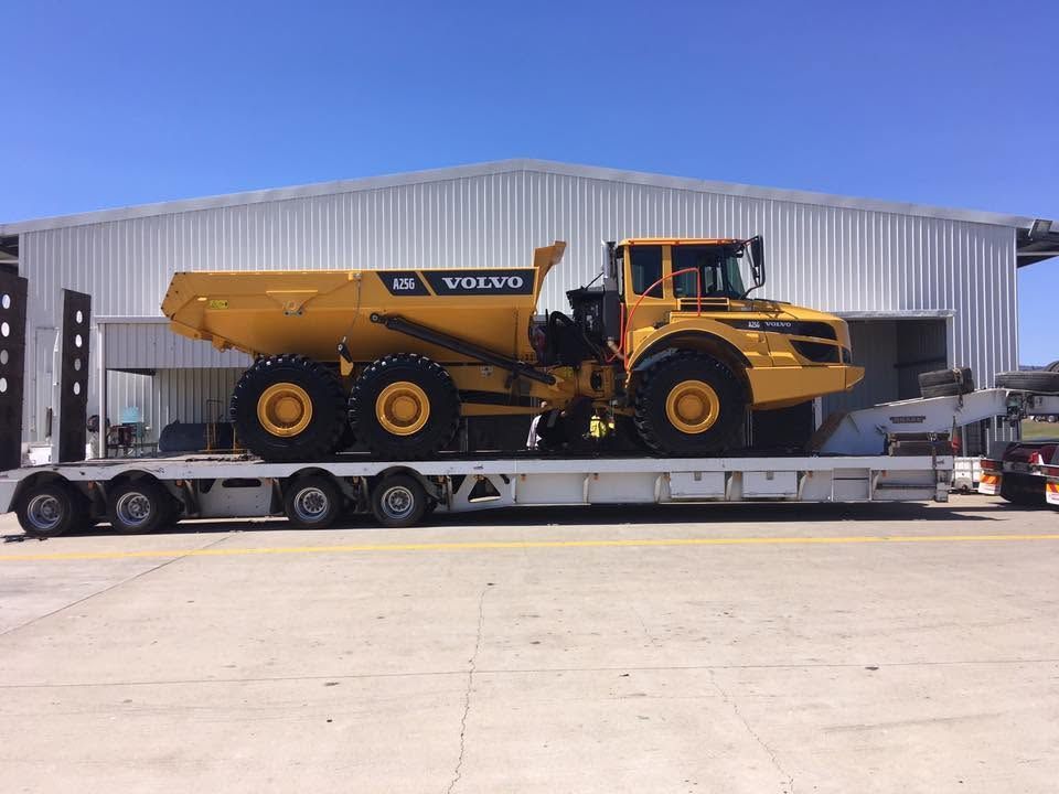 Yellow Volvo Dump Truck on a Flatbed Trailer Outside an Industrial Building — Barlow's Earthmoving in Coorooman, QLD