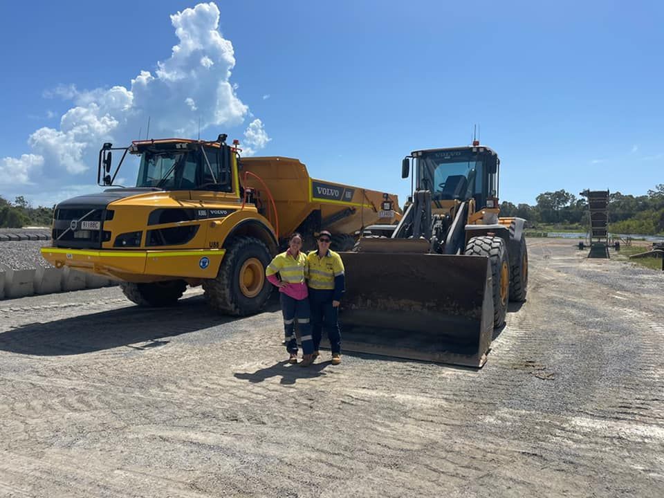 Two Women Stand in Front of Large Yellow Construction — Barlow's Earthmoving in Coorooman, QLD