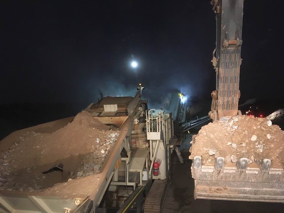 An Excavator Dumping Dirt Into a Rock Crusher at Night — Barlow's Earthmoving in Coorooman, QLD