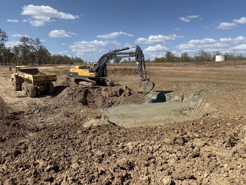 Excavator and Dump Truck Working in A Brown Dirt Field on A Sunny Day — Barlow's Earthmoving in Emu Park, QLD