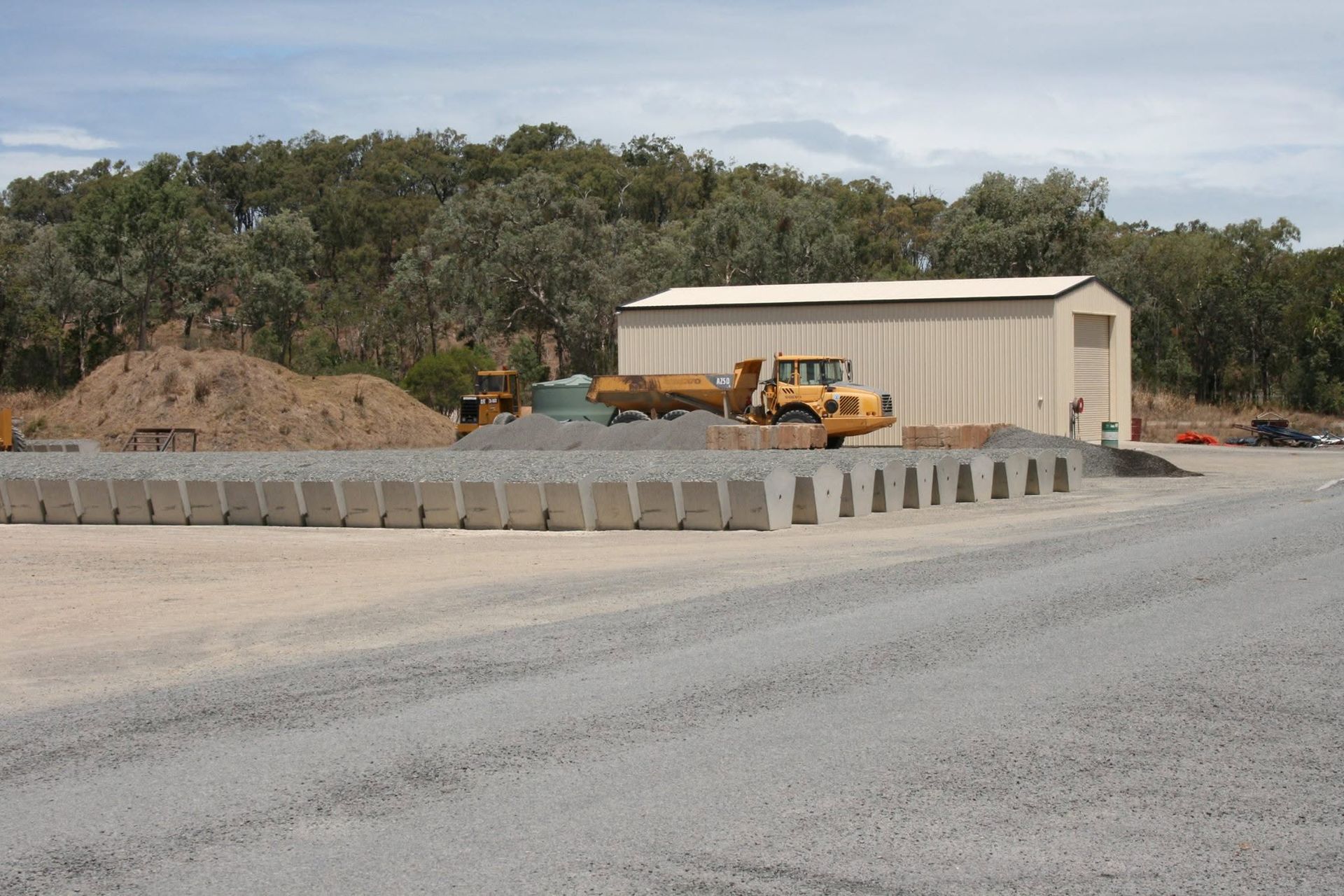 Construction Site With Concrete Barriers, Yellow Machinery, and a Beige Shed — Barlow's Earthmoving in Coorooman, QLD