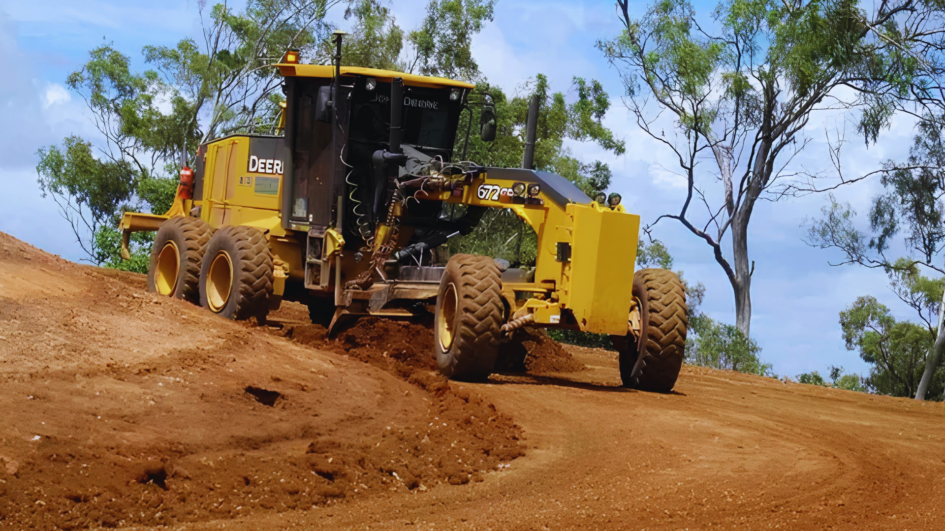 Yellow road grader leveling a dirt road on a rural hillside — Barlow's Earthmoving in Coorooman, QLD