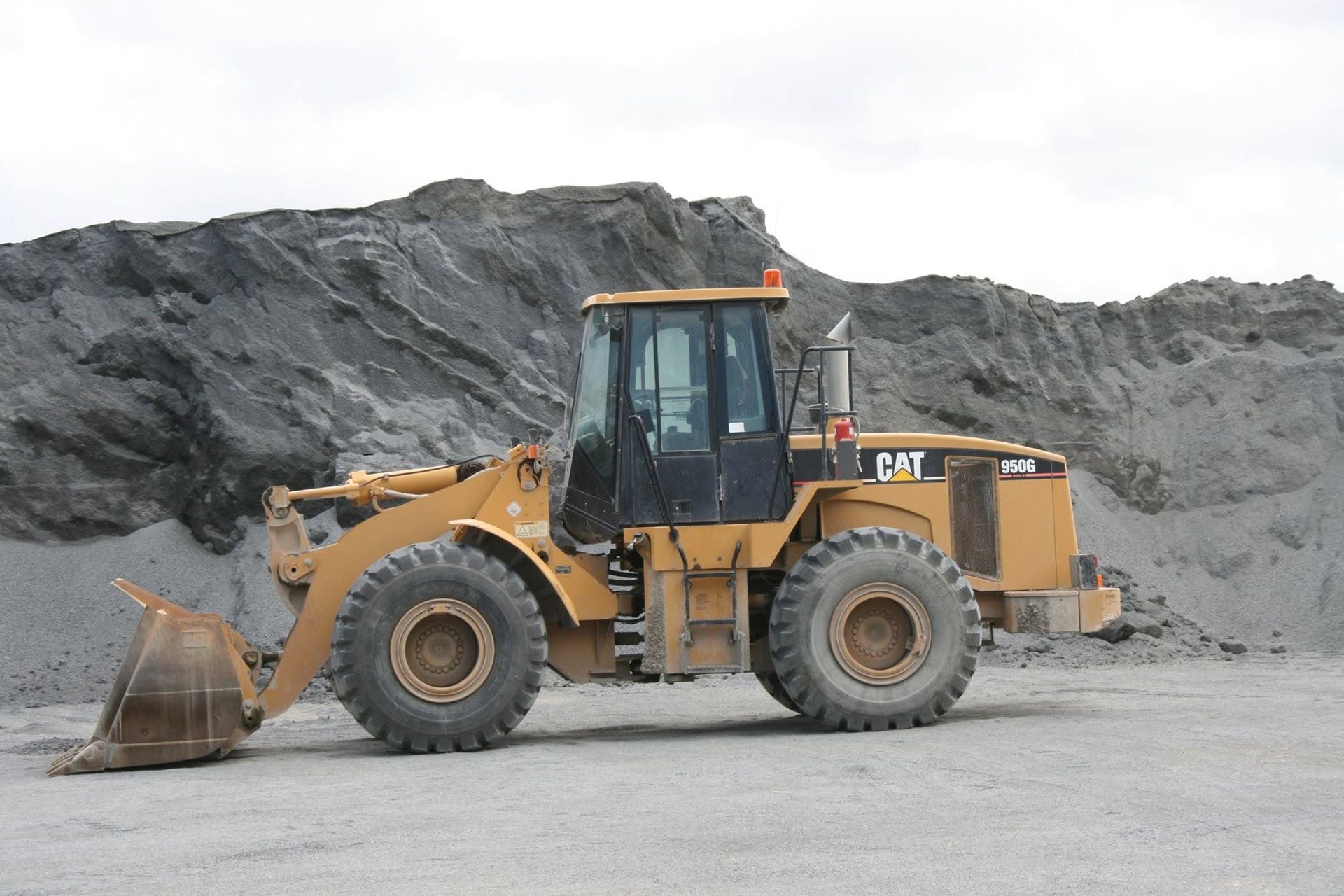 Yellow Front Loader Parked on Gravel in a Gray Quarry, With a Large Pile — Barlow's Earthmoving in Coorooman, QLD