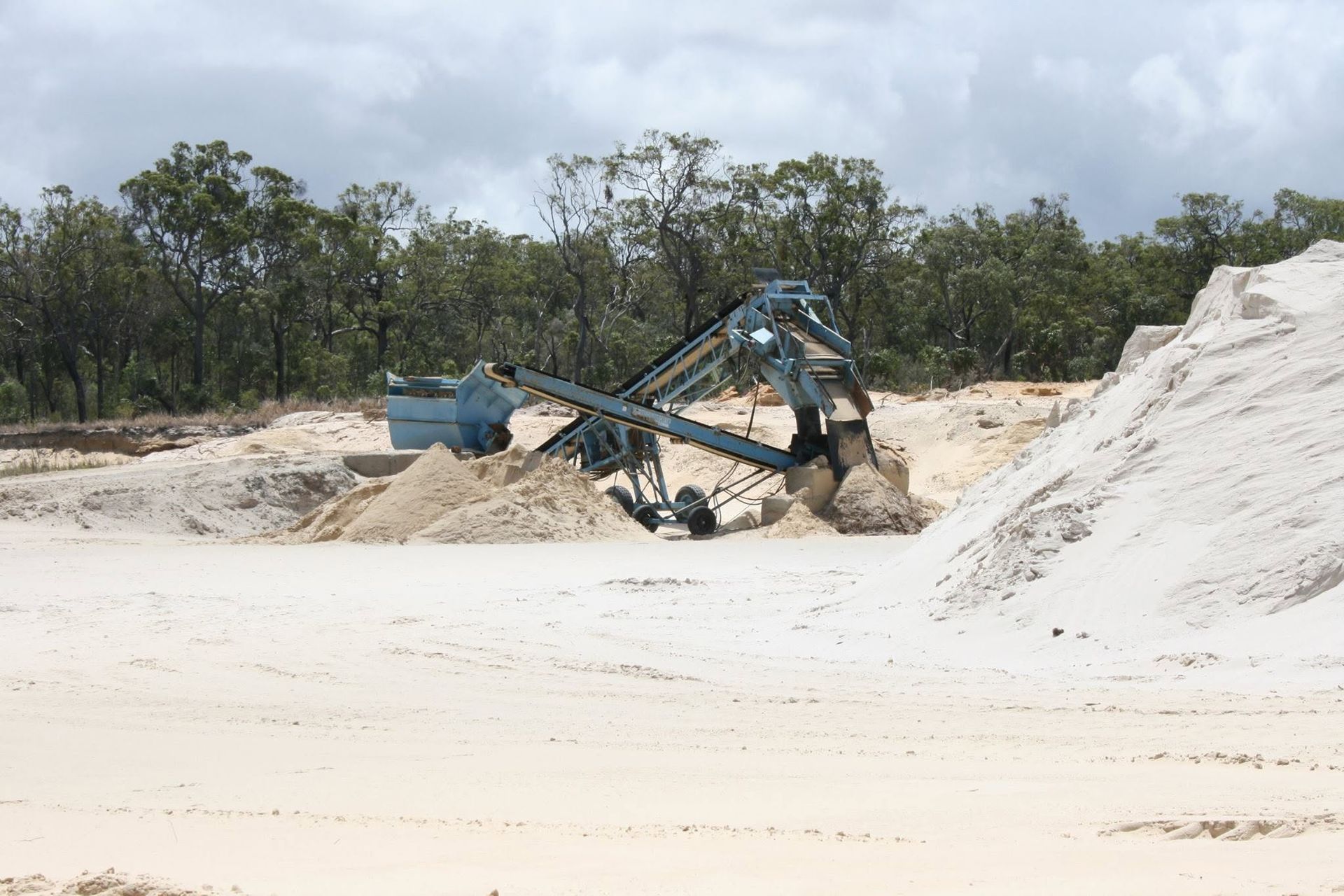 Blue Excavator Moving Sand at a Beach With White Dunes and Trees in the Background — Barlow's Earthmoving in Coorooman, QLD
