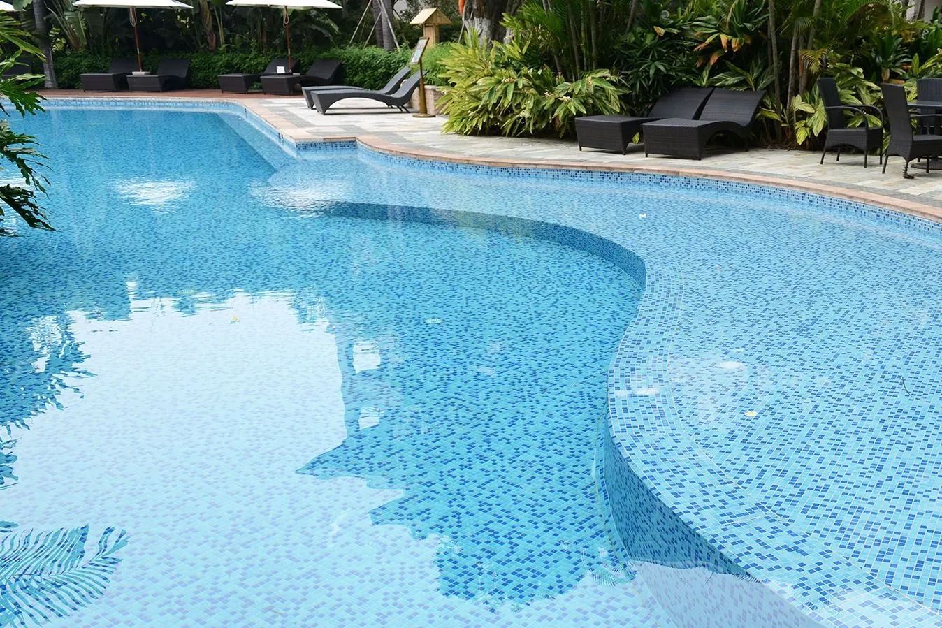 A blue tiled swimming pool with a unique curved design and surrounding lounge chairs.