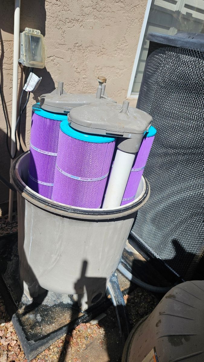 Pool filter with three purple cylindrical filters inside a gray container, outdoors.