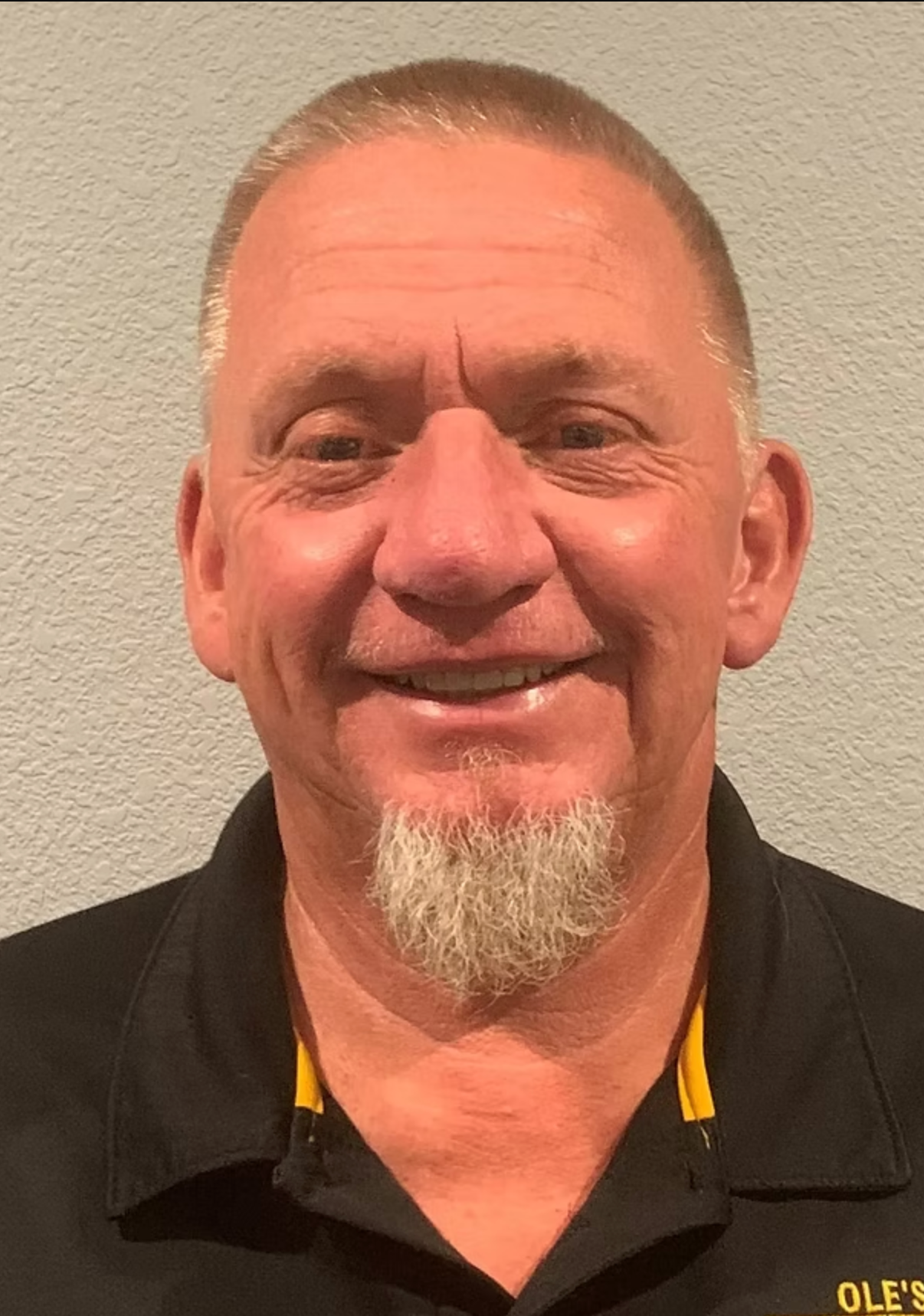 A man with a beard is wearing a black shirt and smiling.