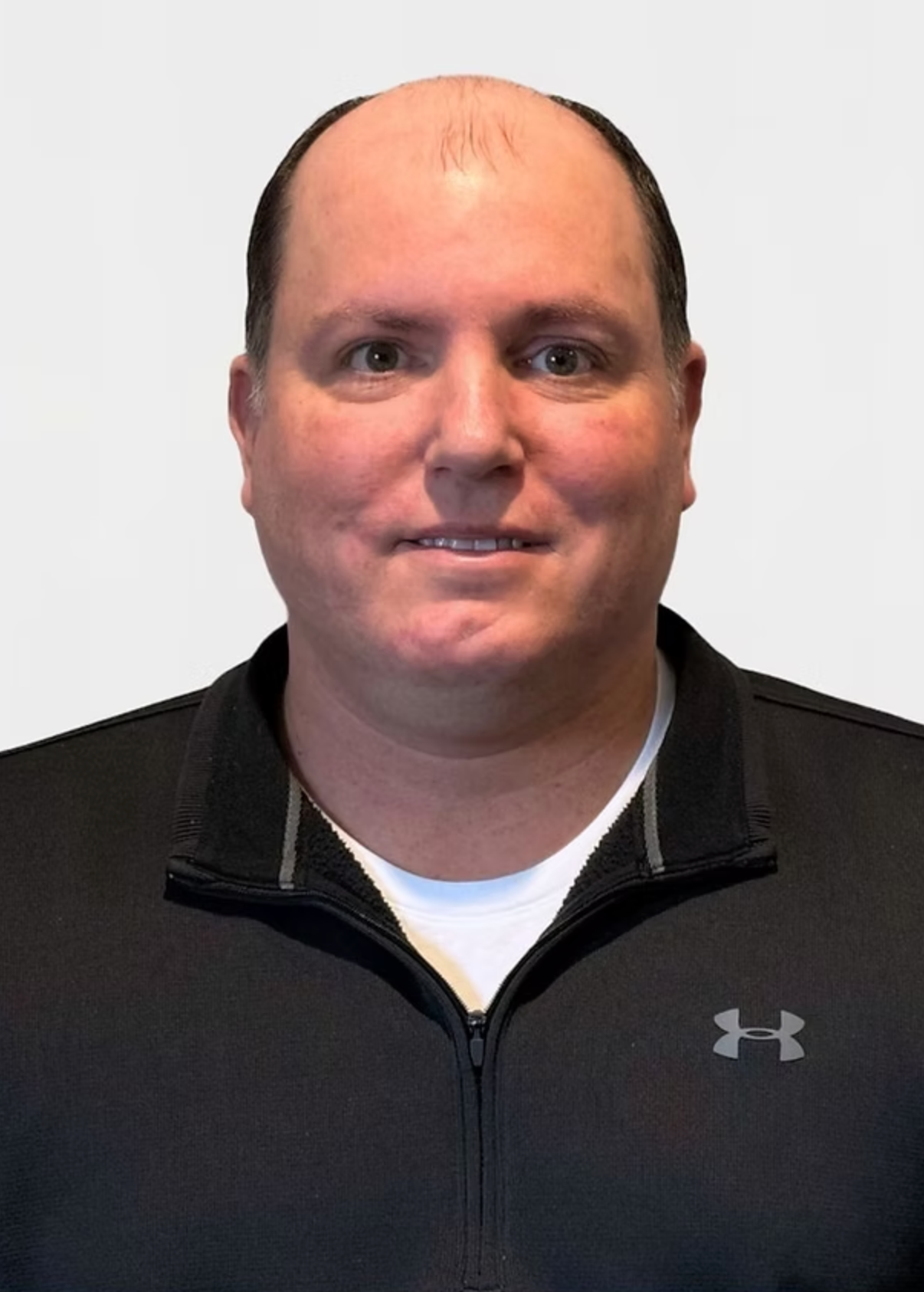 A bald man wearing a black under armour jacket
