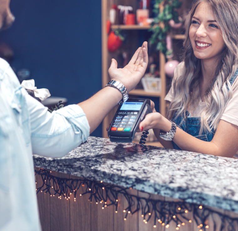 A woman is using a credit card machine to pay a man at a counter.