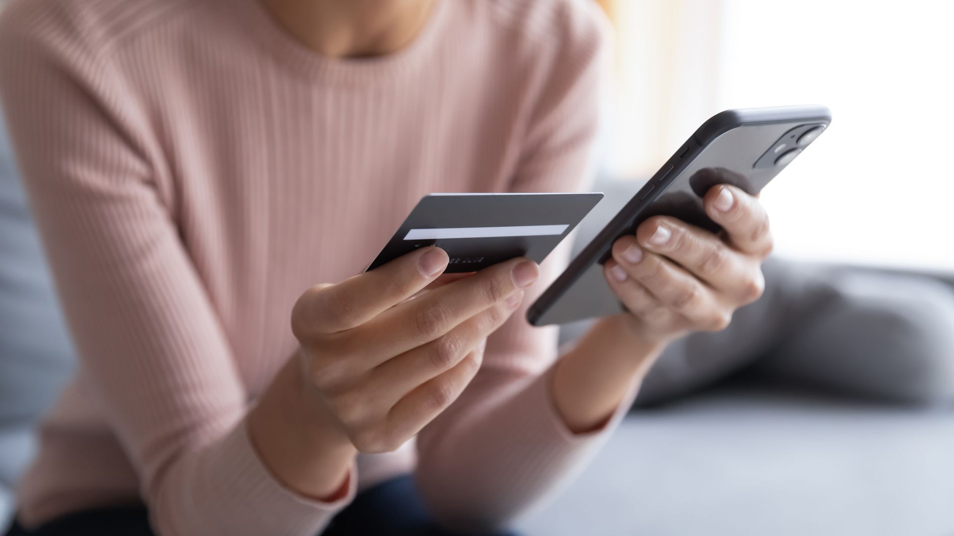 A woman is holding a credit card and a cell phone.