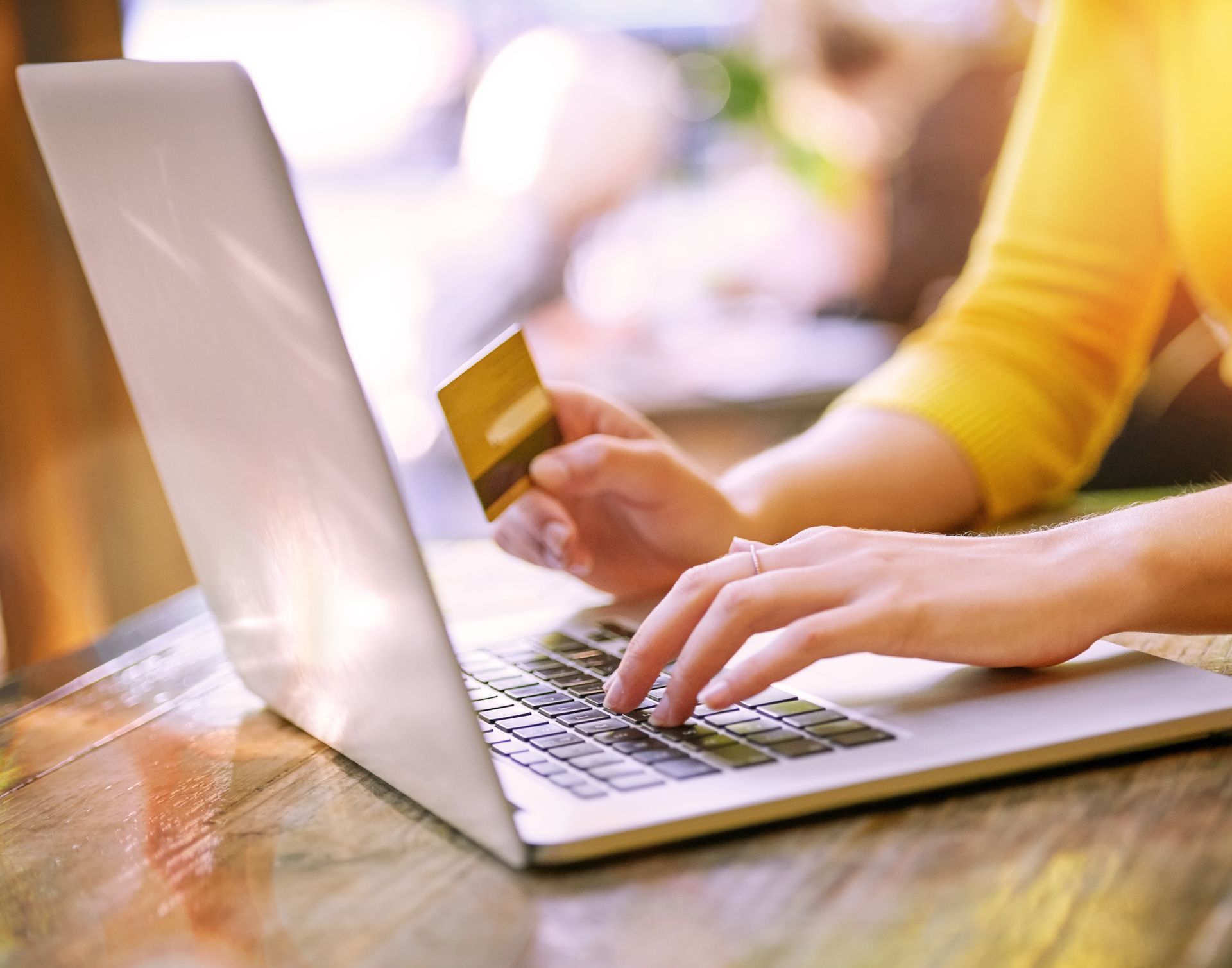 A woman is holding a credit card while typing on a laptop computer.